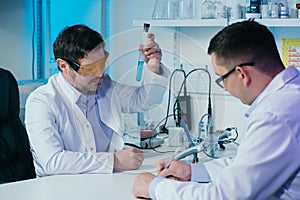 Male scientist in lab working in pharmaceutical studies and medical research with microscope and liquids in test tubes.