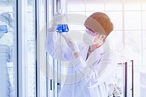 Male scientist looking at flask with blue liquid