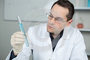Male scientist looking at test tube containing blue liquid