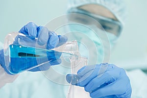 Male Scientist in PPE Suit working in Lab while Pouring Solution from Erlenmeyer Flask to Erlenmeyer Flask with Caution.