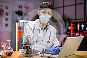 Male scientist in protective mask and gloves testing experiment in science lab using laptop computer