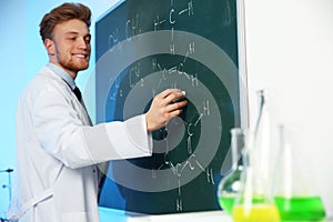 Male scientist writing chemical formula on chalkboard