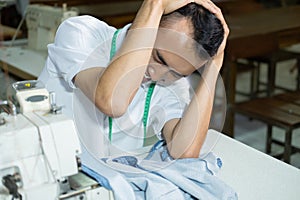 Male seamstress looked down with her head feeling depressed while sewing