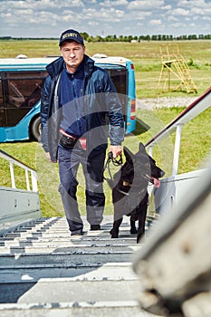 Male security officer with black dog climbing aircraft steps
