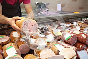 Male seller holding piece of deli meat in butcher shop