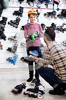 male seller putting roller-skates on boy customer in sports store