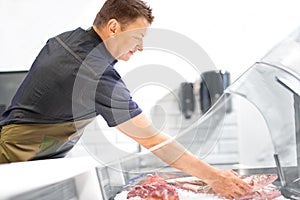 Male seller with seafood at fish shop fridge