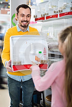 Male seller showing cage with canary bird to girl in pet shop