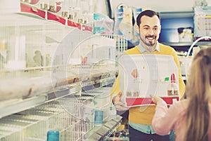 Male seller showing cage with canary bird to girl in pet shop