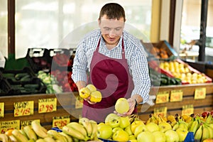 Male seller of vegetable department of store replenishing showcase with apple, put ones on showcase