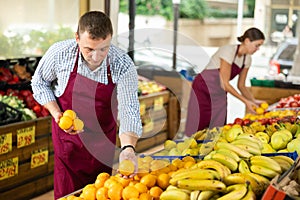 Male seller of vegetable department of store is replenishing showcase with oranges