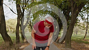 Male senior person running along road in park, using smart watch, tracking result fitness workout