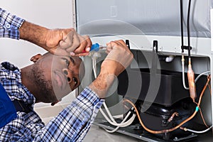 Male Serviceman Working On Fridge With Screwdriver