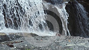 Male shoes standing on stones on flowing waterfall in mountain. Tourist man bathing in mountain waterfall. Handsome man