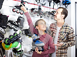 Male shop assistant helping boy to choose roller-skates in sports store