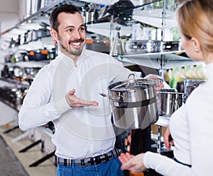 Male shop assistant helping customer to choose saucepan