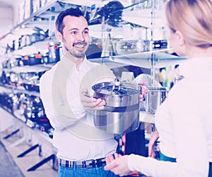 Male shop assistant helping customer to choose saucepan