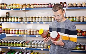 Male shopper selects and buys a jar of pickled cucumbers and tomatoes in grocery supermarket