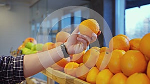 male shopper of supermarket is choosing organic orange in grocery, closeup of hand with fruit