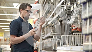 Male shopper is taking big metal drill bit from racks in a shop for builders