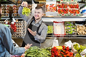 male shopping assistant helping customer to buy fruit and vegetables in grocery shop