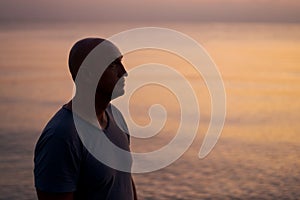 Male silhouette on background sea at sunset looks to side alone. Man enjoying