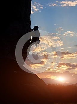 Male silhouette climbing on rock at sunrise. Adrenaline, strength, ambition. Side low angle view. Filtered. Copy space