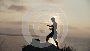 Male silhouette doing morning yoga on the big stone by the sea at sunrise