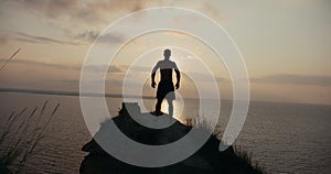 Male silhouette doing squats on the big stone by the sea at sunrise