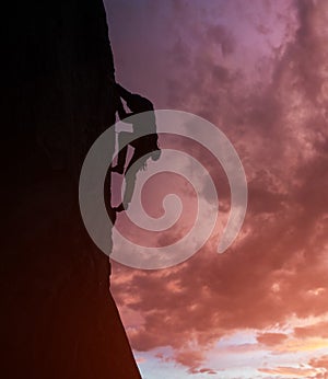 Male silhouette rock climbing, doing next step on cliff. Dark purple cloudy sky on background with copy space. Low angle