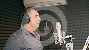 Male singer in headphones singing song into the microphone at sound studio. Show business concept. Adult man recording a