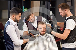 Male sitting in chair while hairdressers servicing him