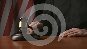 Male sitting at the desk with wooden hammer and law book, USA flag at the background. Man judge in the court room