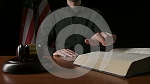 Male sitting at the desk with wooden hammer and law book, USA flag at the background. Man judge in the court room