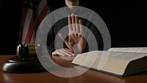 Male sitting at the desk with wooden hammer and law book, USA flag at the background. Man judge in the court room shows