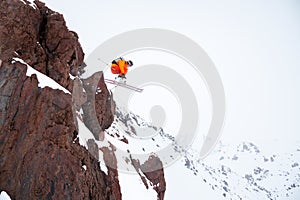 Male skier athlete doing a drop jump from a cliff in the snowy mountains on a cloudy day in winter