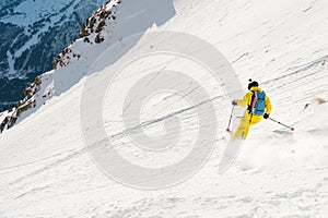 A male skier freerider with a beard descends the backcountry at high speed from the slope