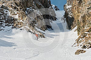 A male skier freerider with a beard descends the backcountry at high speed from the slope