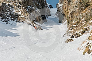 A male skier freerider with a beard descends the backcountry at high speed from the slope