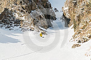 A male skier freerider with a beard descends the backcountry at high speed from the slope