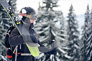 Male skier in goggles with professional ski equipment on his shoulders standing on slope top before skiing in mountains.