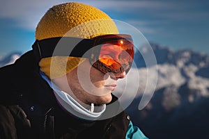 Male skier overlooking snow covered mountains on a sunny day, sun beams reflection in ski goggles
