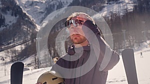 Male skier puts on a mask or sunglasses at a ski resort. Professional sportsman wearing ski glasses