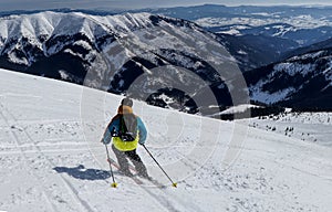 Male skier skiing freeride downhill with view to valley of Low Tatras, Slovakia. Colorful jacket with black backpack