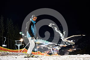 Male skier standing on snowy hill at night.