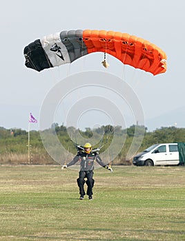 Male skydiver making safe landing landing on grass with open bright colourful parachute.