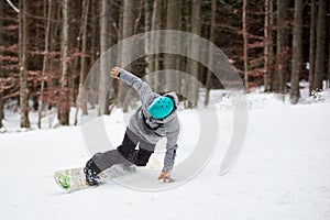 Male snowboarder in blue helmet, risky sliding on flat snow-covered road. Tree trunks and dark forest on background.