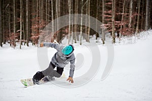 Male snowboarder in blue helmet, risky sliding on flat snow-covered road. Tree trunks and dark forest on background.