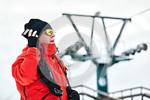 Male snowboarder resting on the slope of the hill, talking on the phone on a beautiful sunny winter day at ski resort