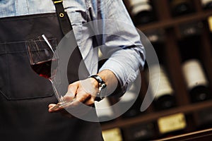 Male sommelier holds bokal with red wine in hand